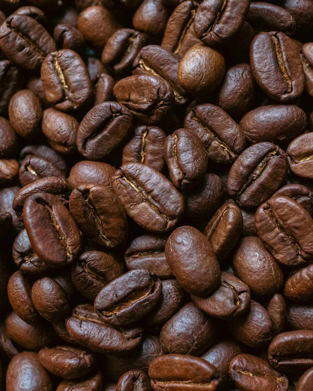A close-up, top-down view of roasted coffee beans filling the entire frame, showing their rich dark brown color and glossy texture.