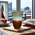 Decorative glass vase on a table with a candle and books in the background