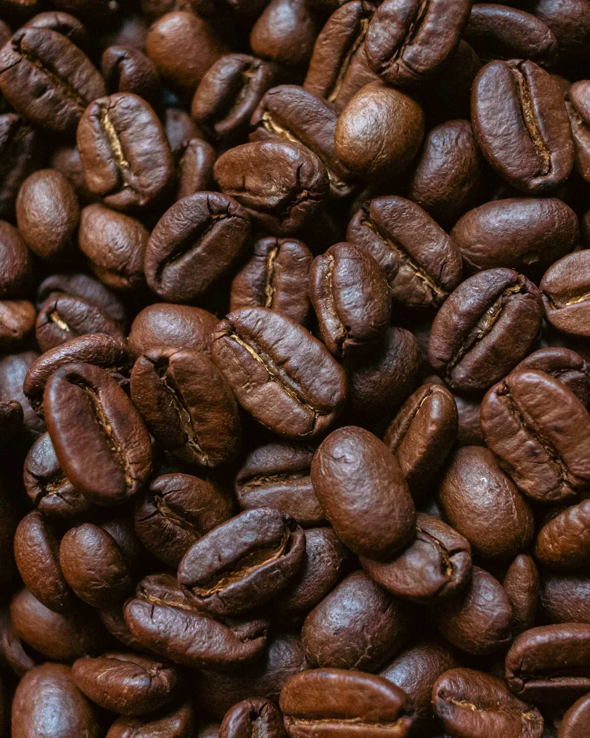 A close-up, top-down view of roasted coffee beans filling the entire frame, showing their rich dark brown color and glossy texture.