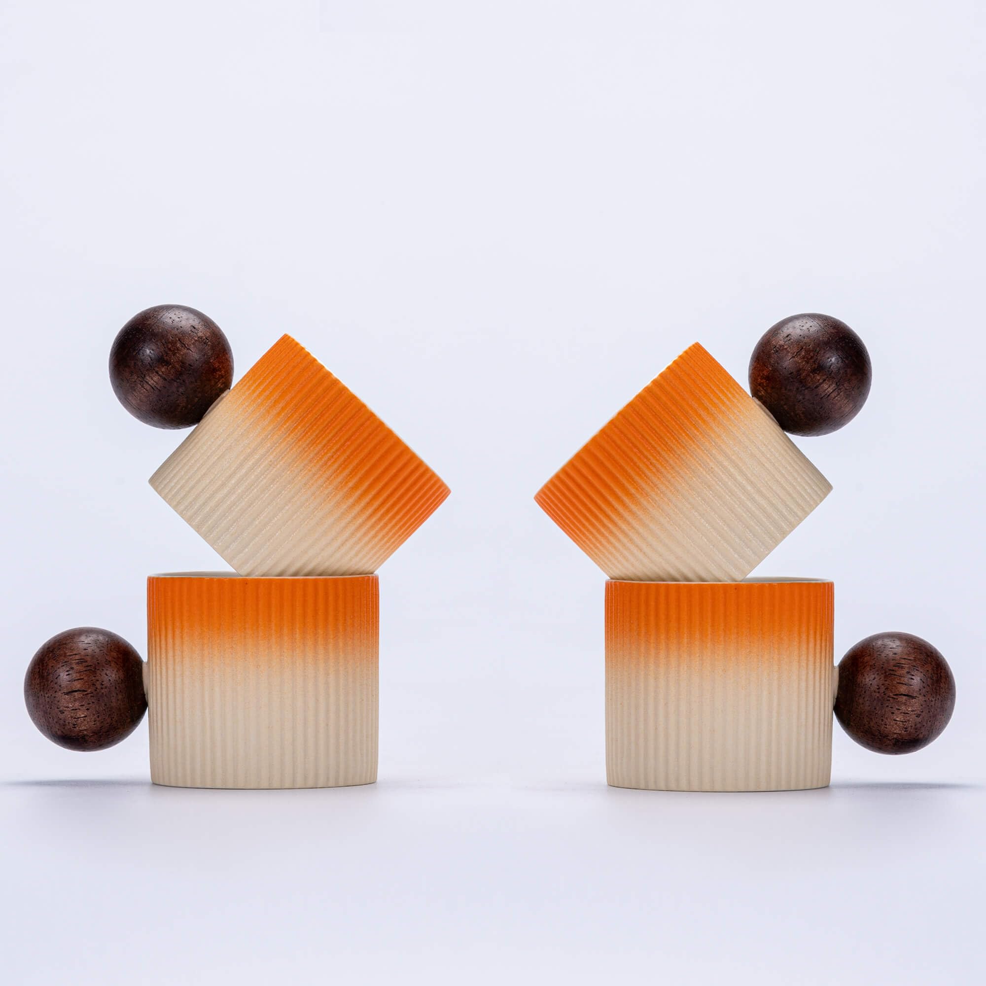 Two matching ribbed decorative objects with orange-to-cream gradient tops and bottoms, arranged symmetrically on a white studio background with dark brown spherical accents.