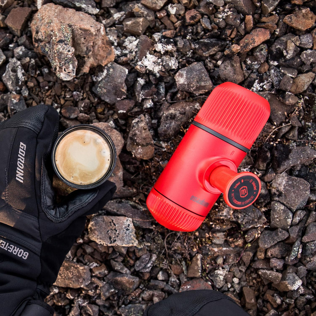 Red portable coffee maker and a cup of coffee on rocky ground