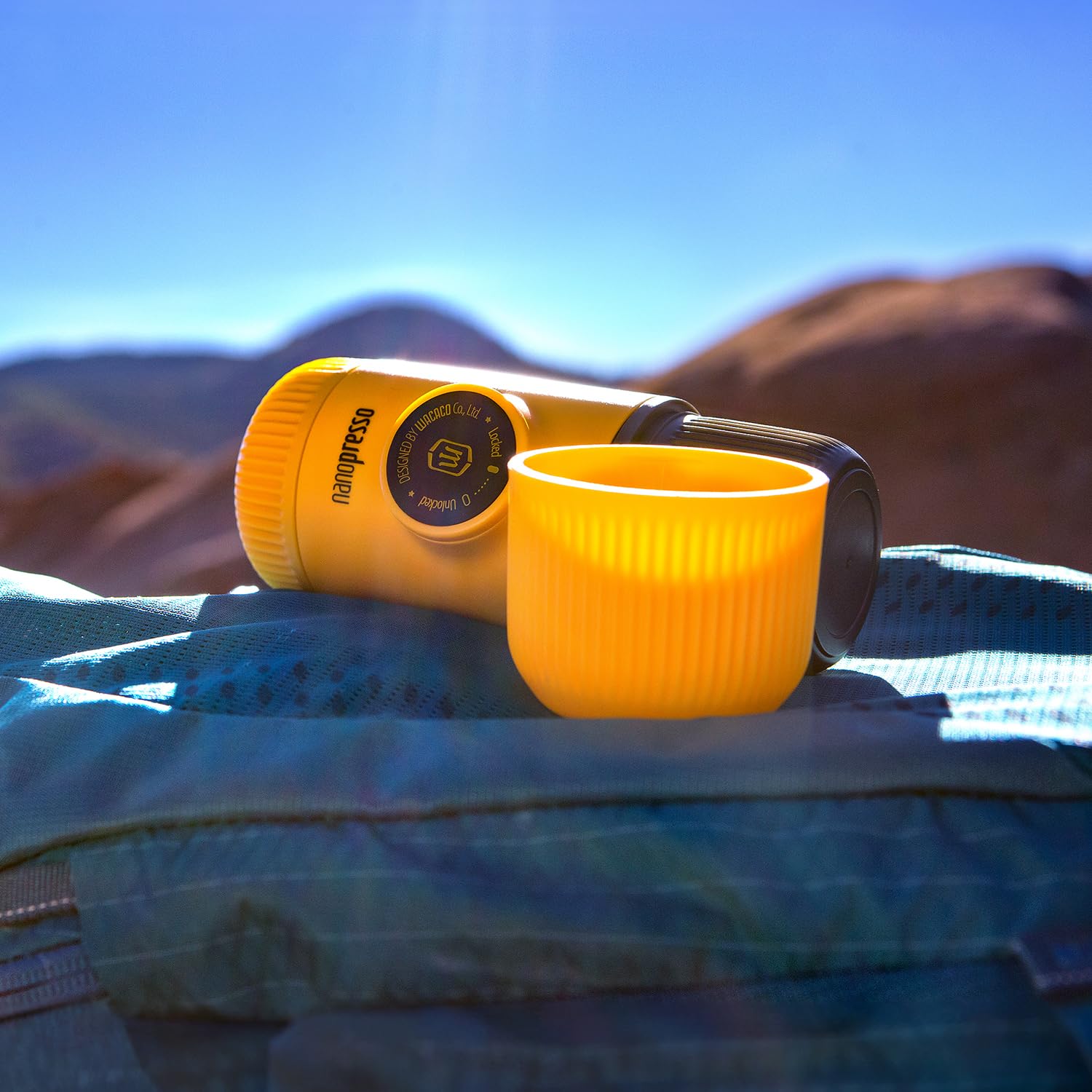 Yellow camping lantern and mug on a blue blanket with desert landscape in the background