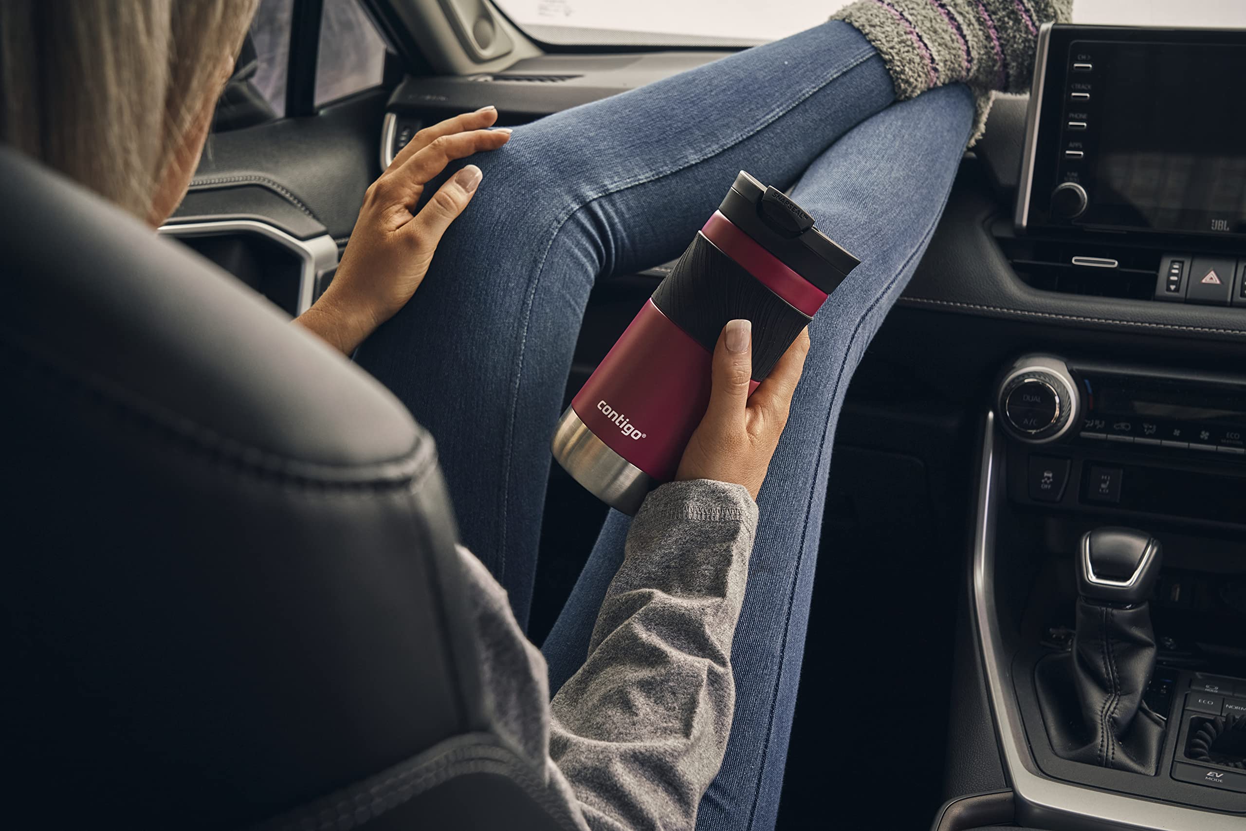 Person holding a red and black cup in a car, with a focus on the cup.