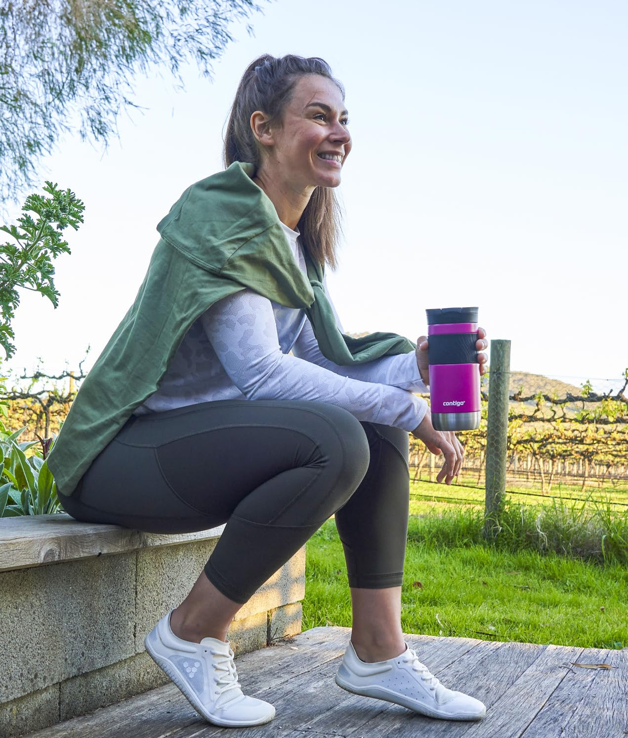 Woman sitting outdoors holding a pink water bottle with text about patented technologies for drinking.