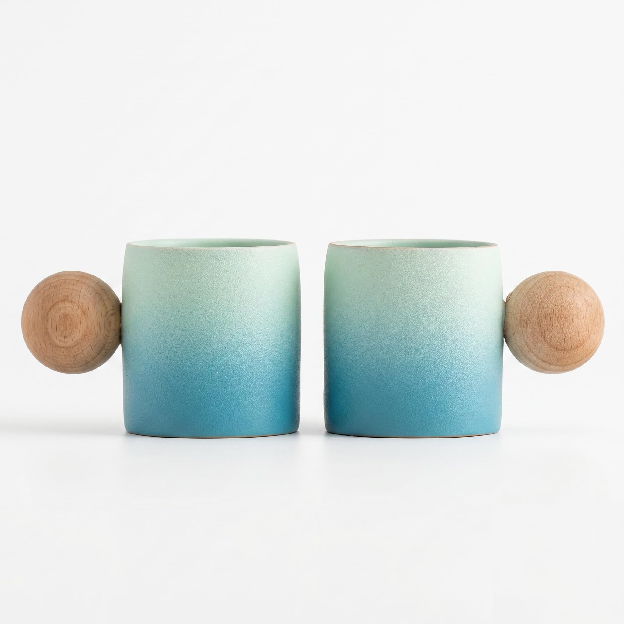 Two ceramic mugs with a light green to blue gradient glaze and natural wood ball handles, shown on a clean white background.