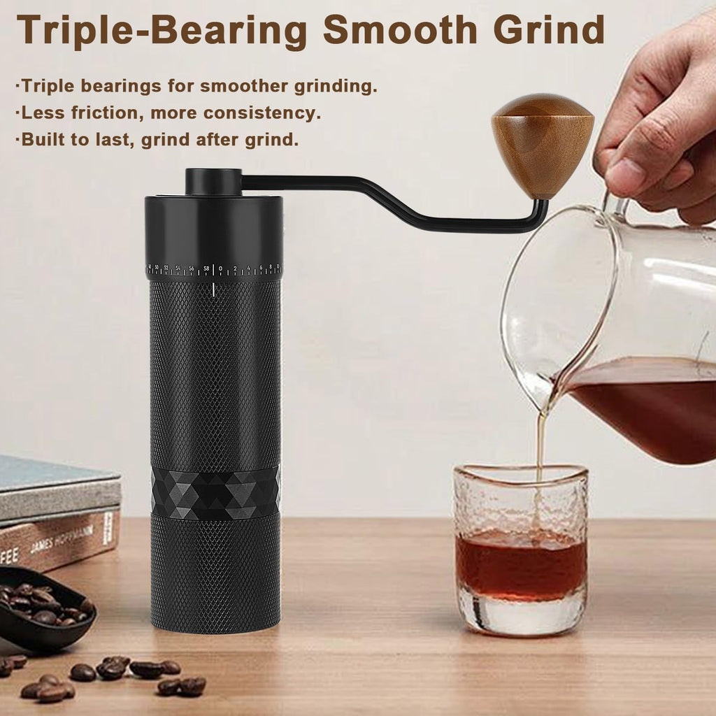 A black manual coffee grinder with a wooden-handled crank is shown on a tabletop, with coffee being poured from a glass carafe into a small glass cup. Text on the image highlights triple-bearing smooth grinding benefits.