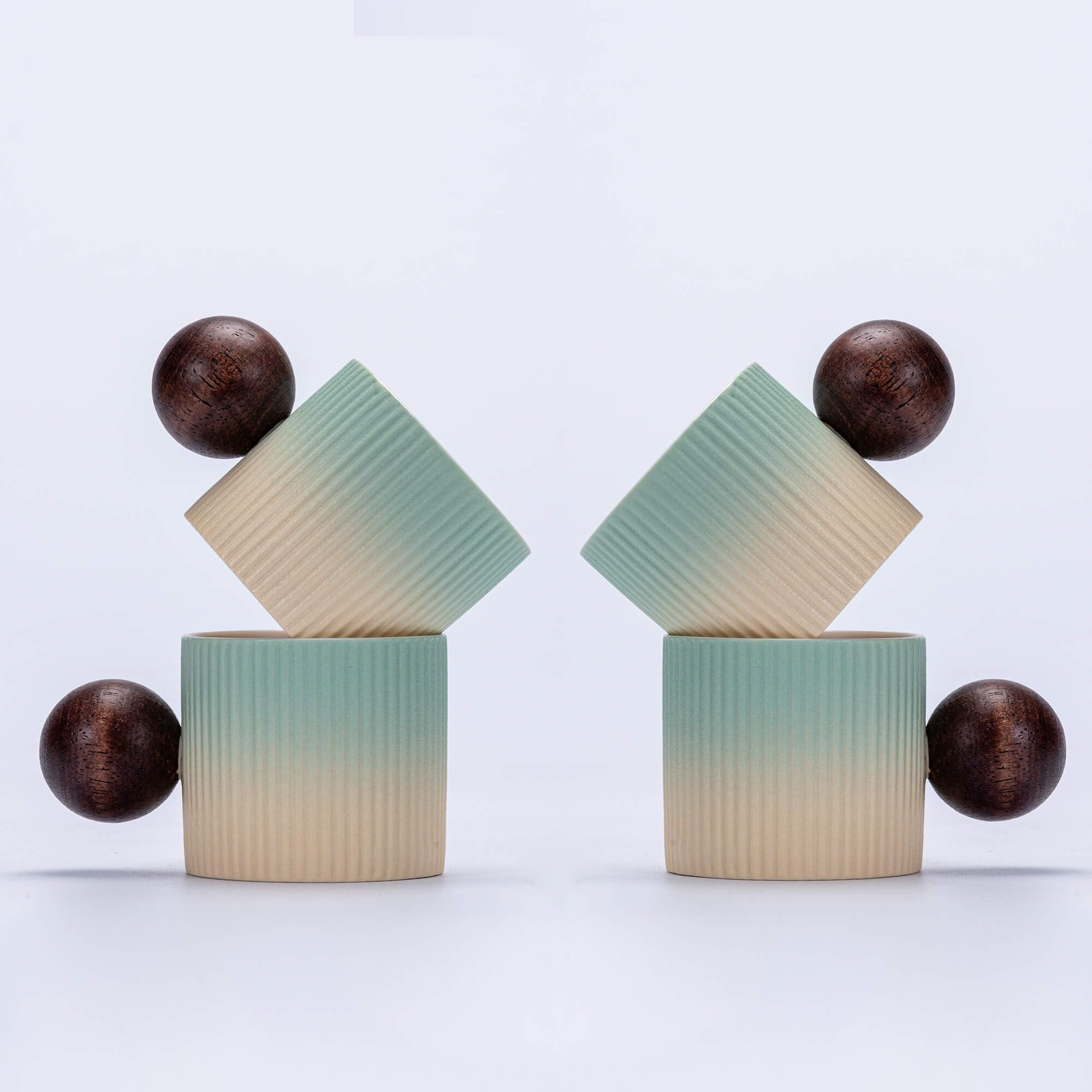 Two matching ribbed ceramic geometric sculptures on a white background. Each sculpture features a cylindrical base in a vertical ombré transition from dark brown to light beige, with a diamond-shaped top piece in the same ombré, and two spherical dark brown accents on either side.
