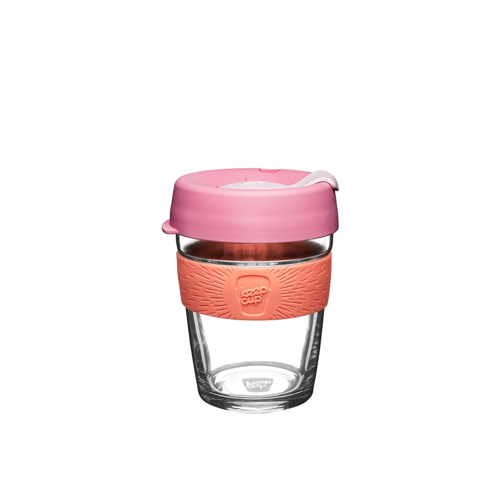A reusable glass travel tumbler with a translucent pink lid, a textured coral-pink silicone sleeve, and a clear glass body, shown on a plain white background.